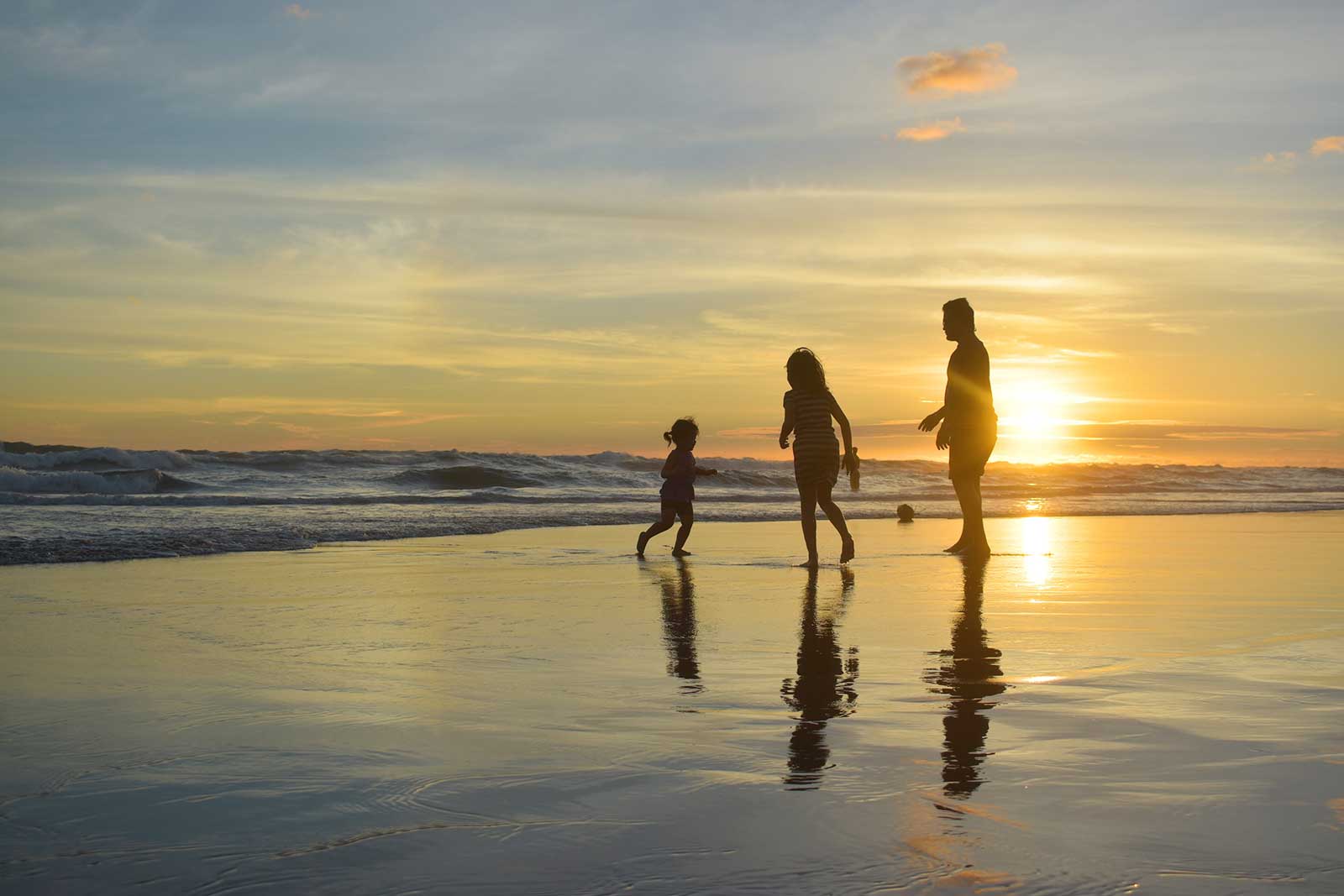 Family enjoying a sunset walk on the beach with reflections in the wet sand.