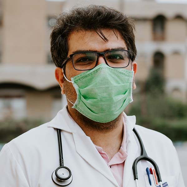 Medical professional wearing a green mask and glasses outdoors.