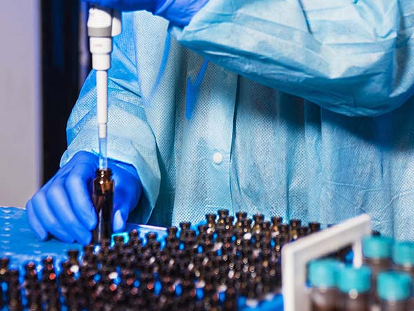 Scientist using a pipette to transfer liquid into small vials in a lab.