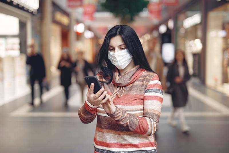 Woman in mask using phone in busy shopping street.