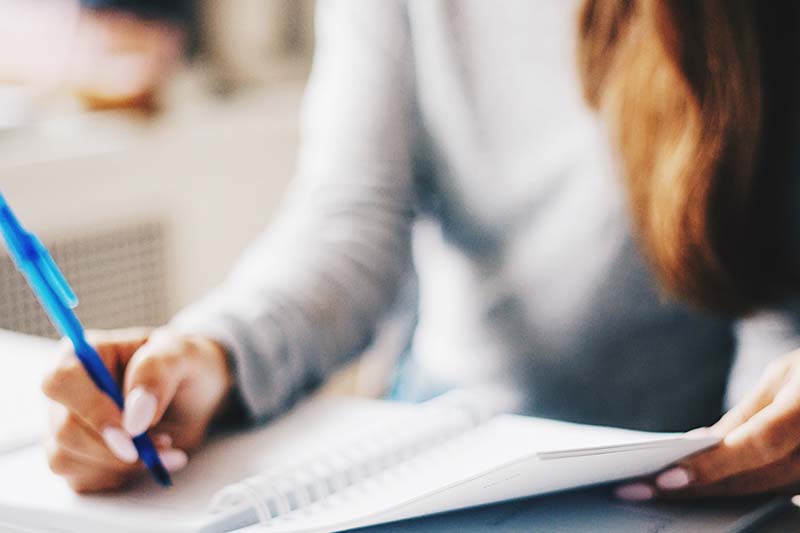 Person writing notes in a notebook with a pen.