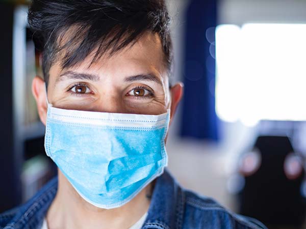 Young man wearing a blue face mask and smiling with eyes.
