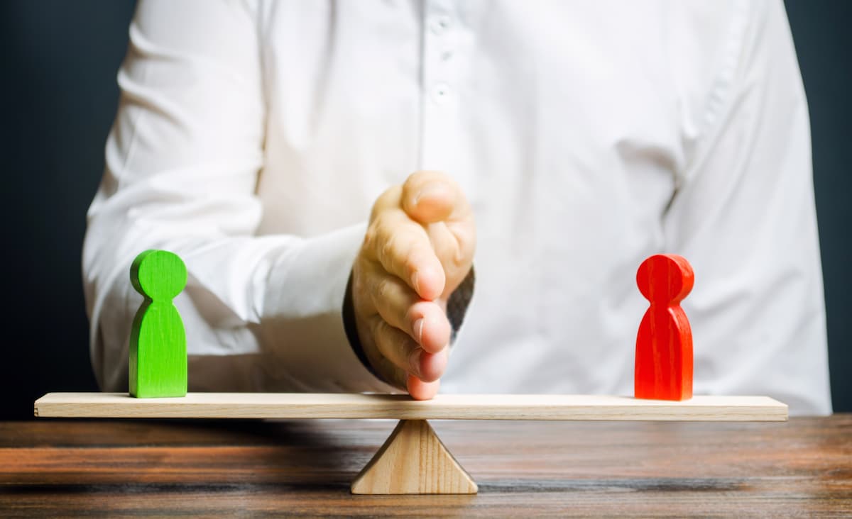 A person balancing two figurines on a seesaw with a hand in the middle.