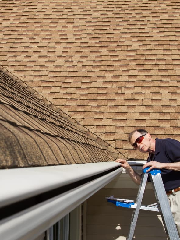 Man cleaning gutters while standing on a ladder outside a house.