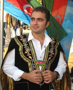 Man in traditional attire, Azerbaijani flags behind.