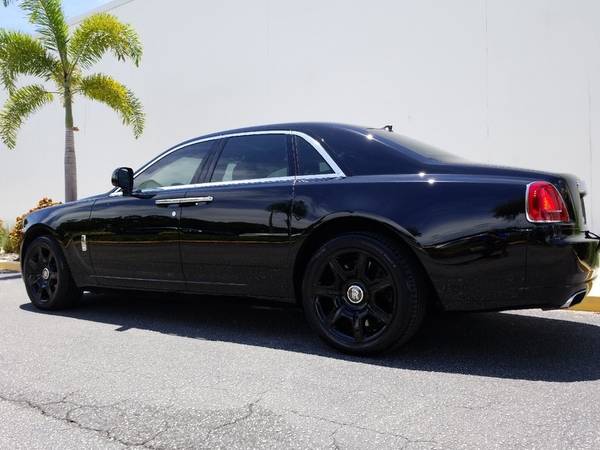 Black luxury car parked near palm tree.