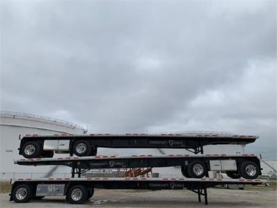 Stacked flatbed trailers under cloudy sky.