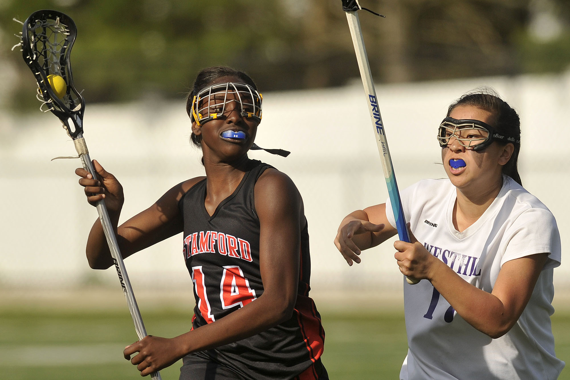 Two women playing lacrosse with mouthguards.